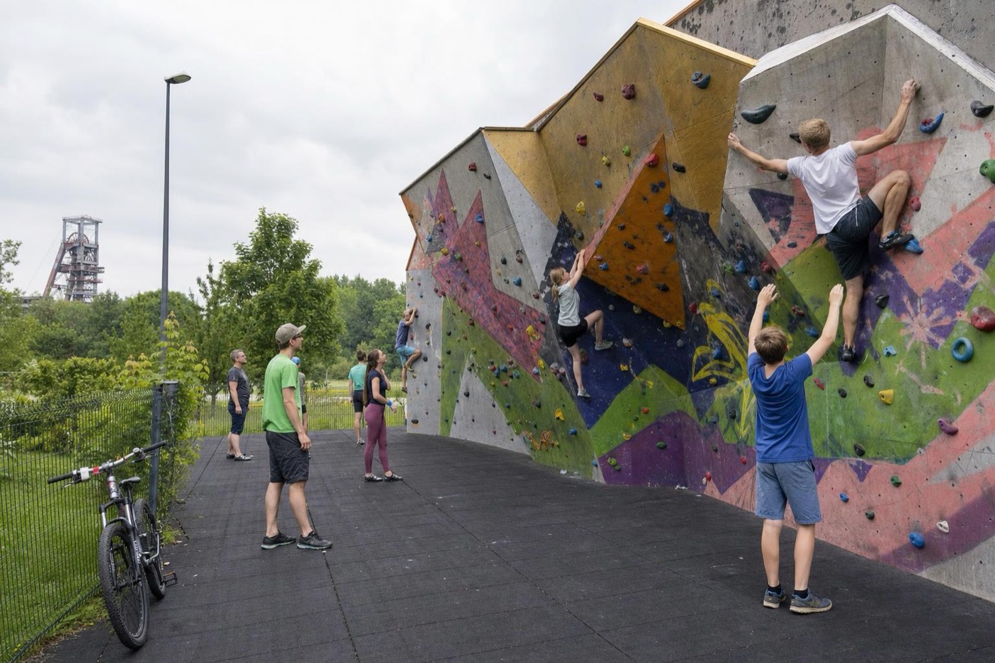 Öffentliche Boulderwand im Park mit bunten Griffen, im Hintergrund ein Förderturm